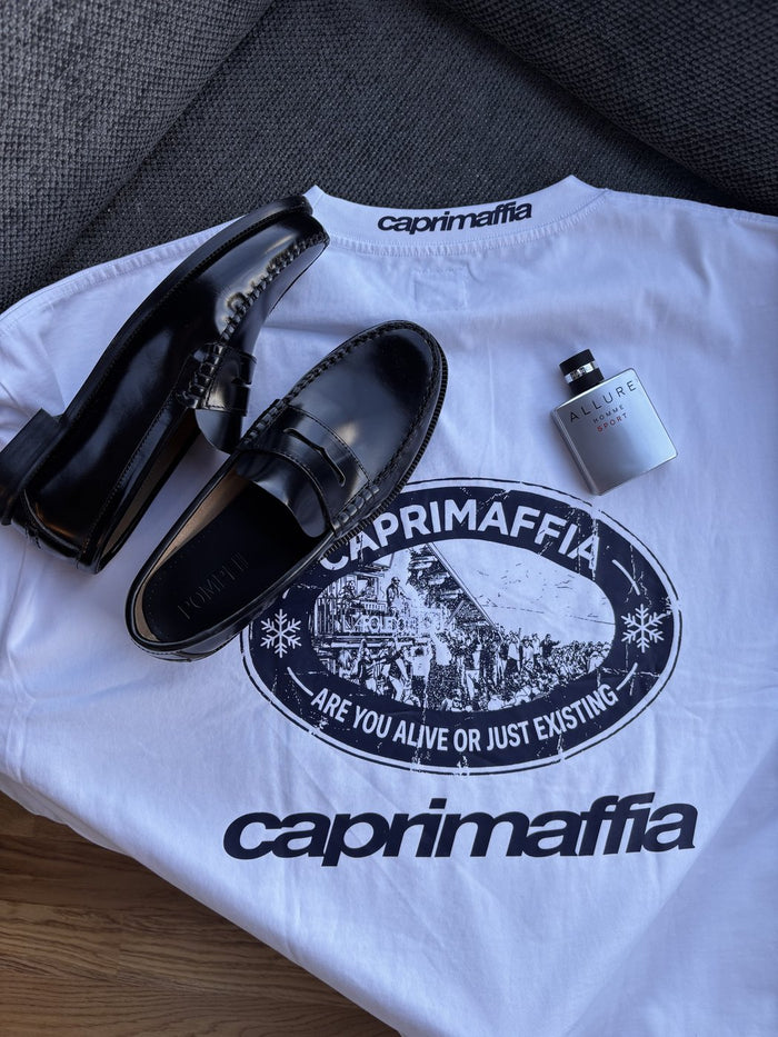 Camiseta de CAPRIMAFFIA y calzado colocados sobre la cama